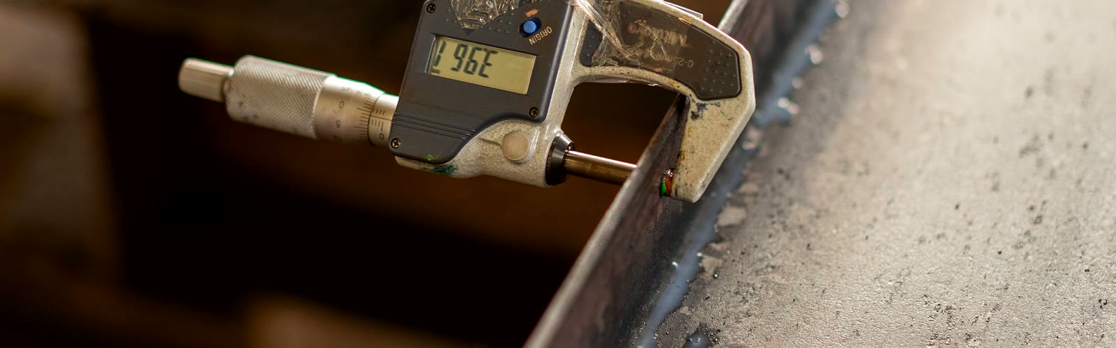 Digital micrometer measuring a machined steel part edge at the inspection bench