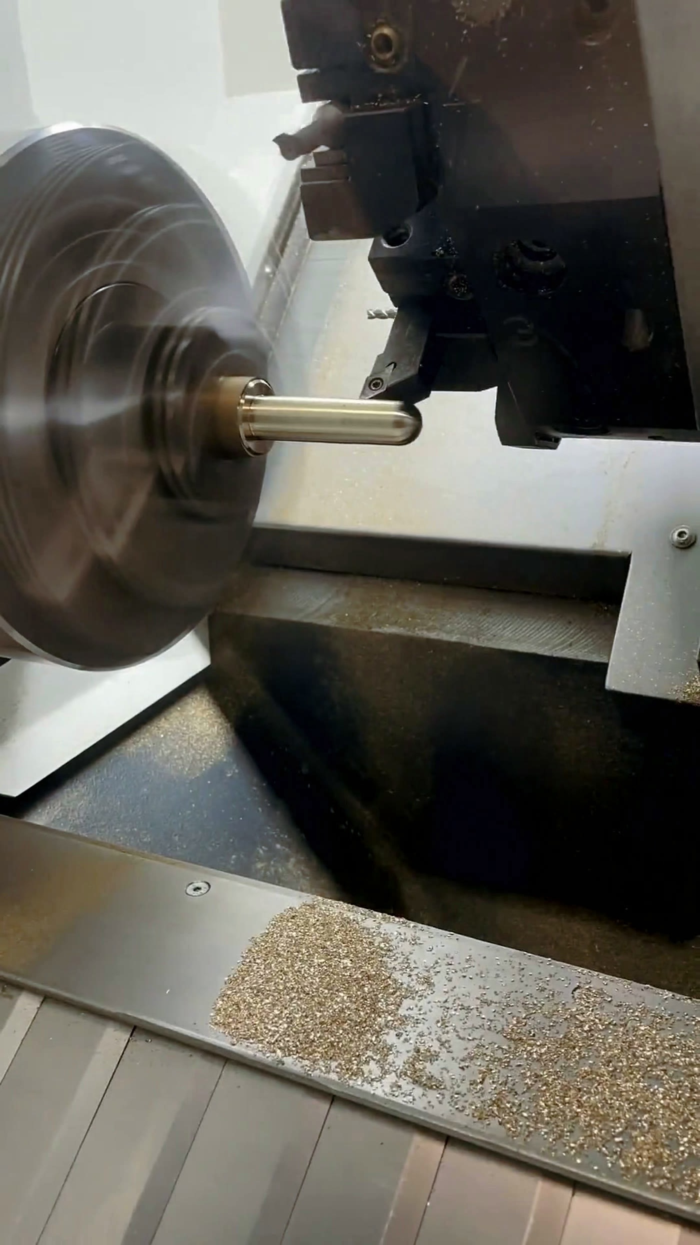 CNC lathe turning a brass workpiece, sharp tool-to-part interface with brass swarf on the ways
