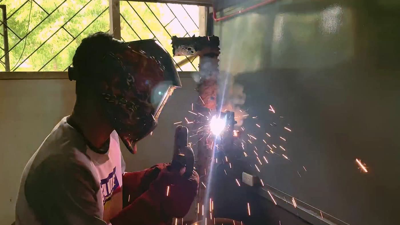 Stick welding a vertical steel post in the fab bay, spark fan off the joint