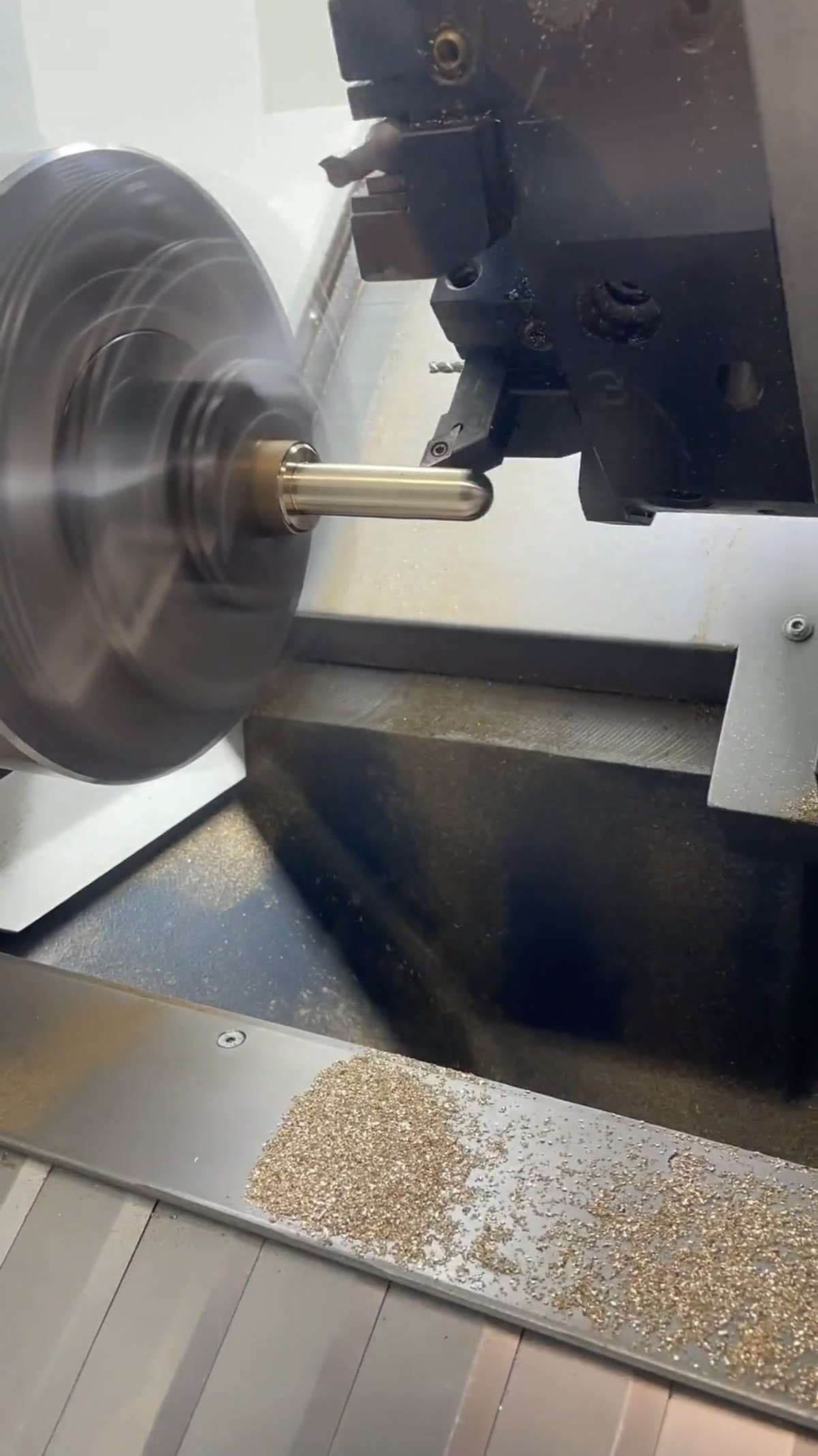 CNC lathe chuck and live tool post turning a brass workpiece, fresh swarf on the bed