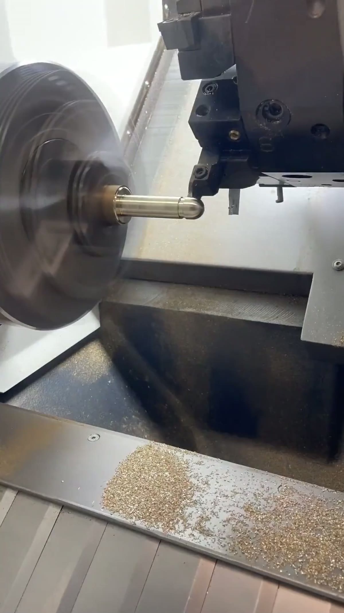 CNC lathe turning a small brass pin, fresh swarf piled in the chip tray