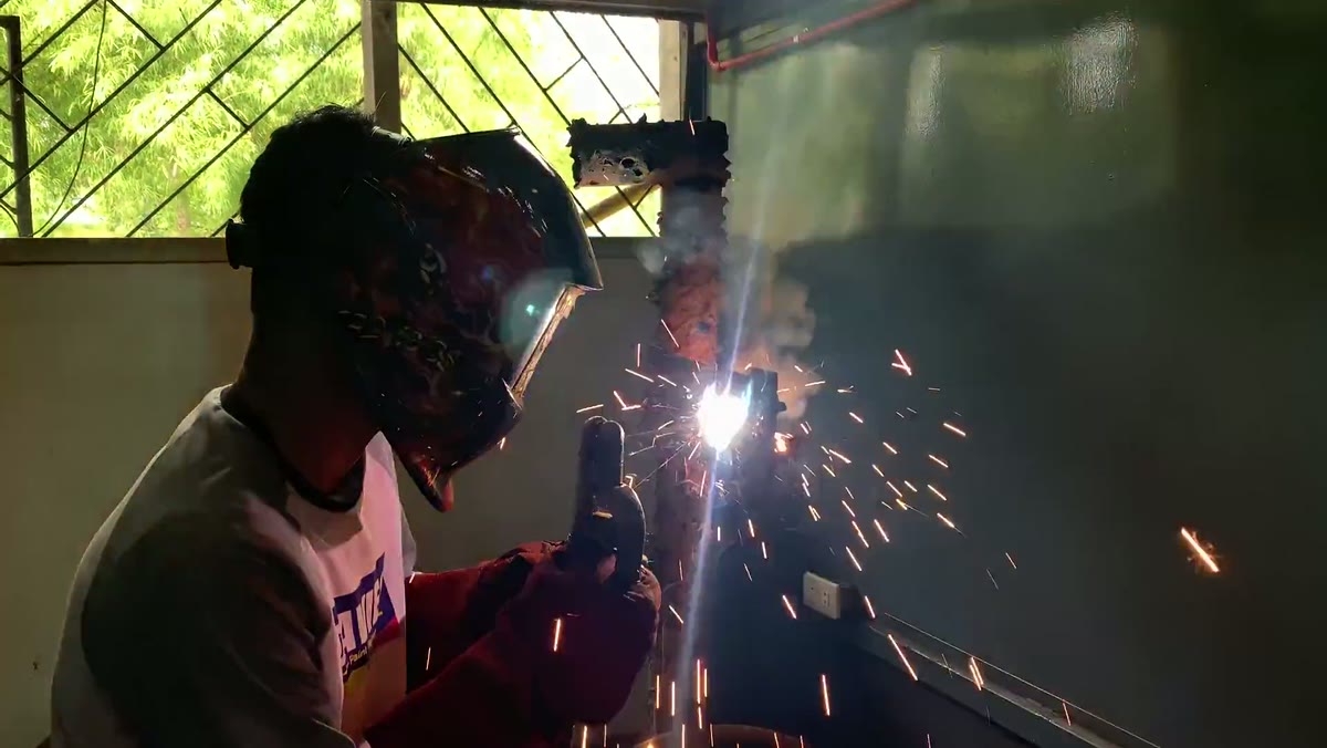 Welder striking an arc, sparks fanning across a dark weld bay
