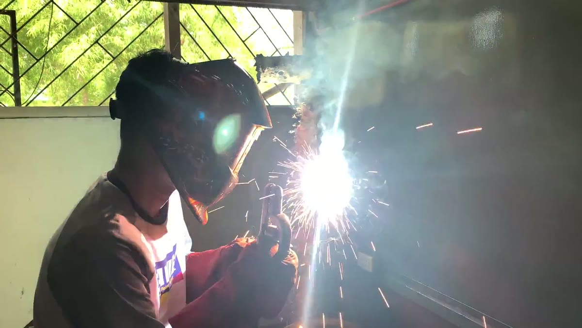 Welder in a flip-lens helmet striking a bright stick-welding arc on the Jacksonville shop floor, sparks bursting off the joint